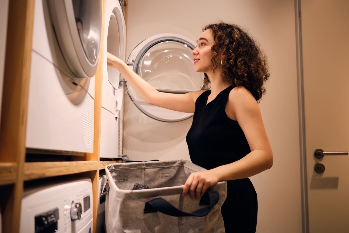 người phụ nữ cho quần áo vào máy giặt