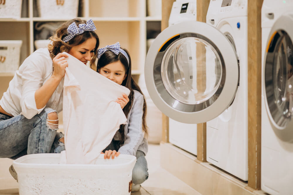 người phụ nữ và đứa trẻ nhìn vào quần áo trắng trong máy giặt